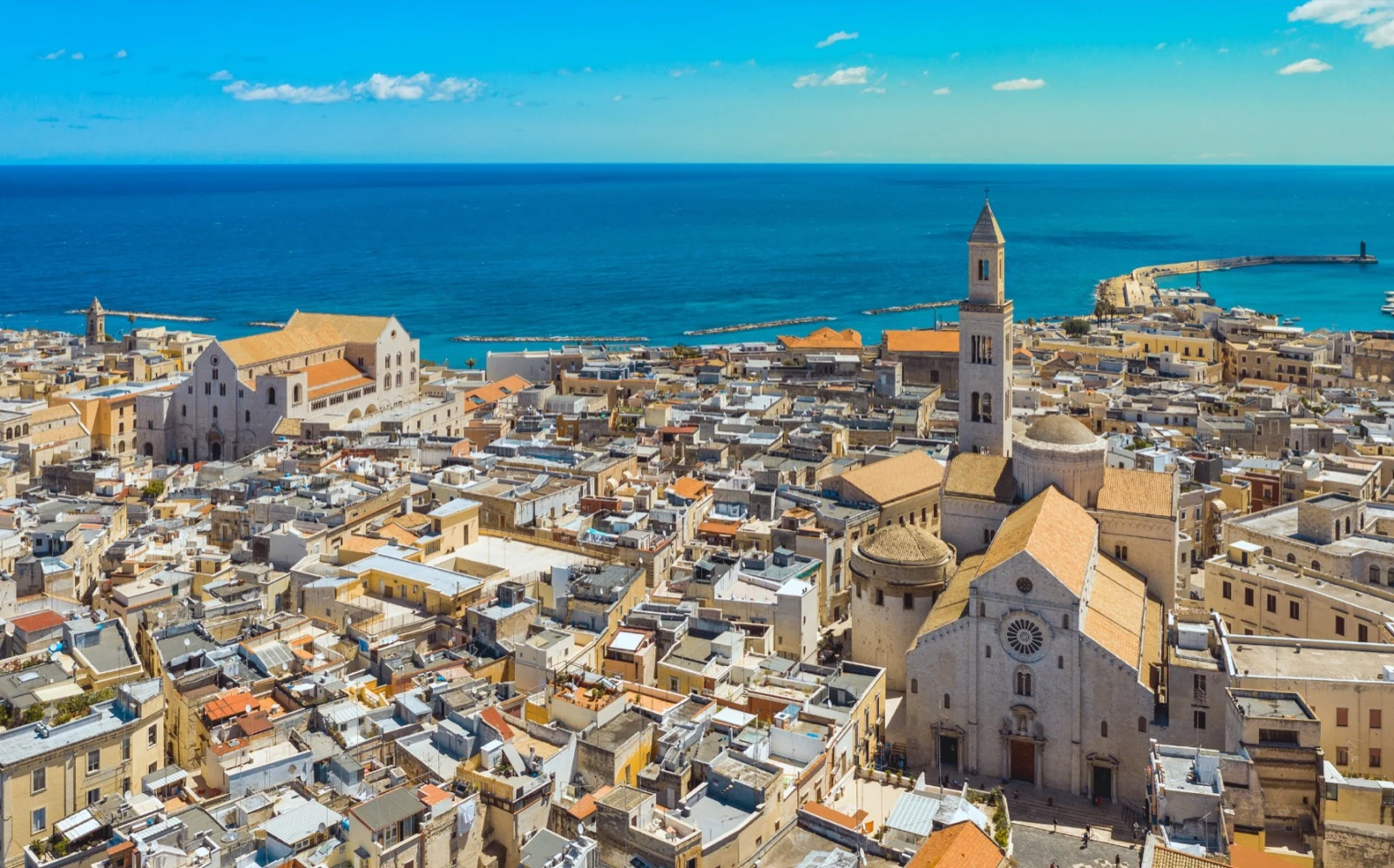 Elevated view over Bari's old town, with stone churches, dense rooftops, the harbour, and the Adriatic Sea